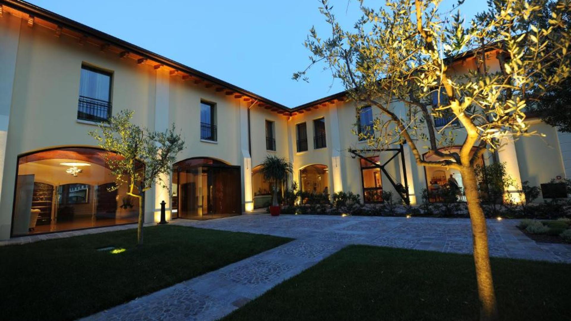 Elegante edificio moderno con giardino, illuminato di sera, con ampie finestre e alberi.