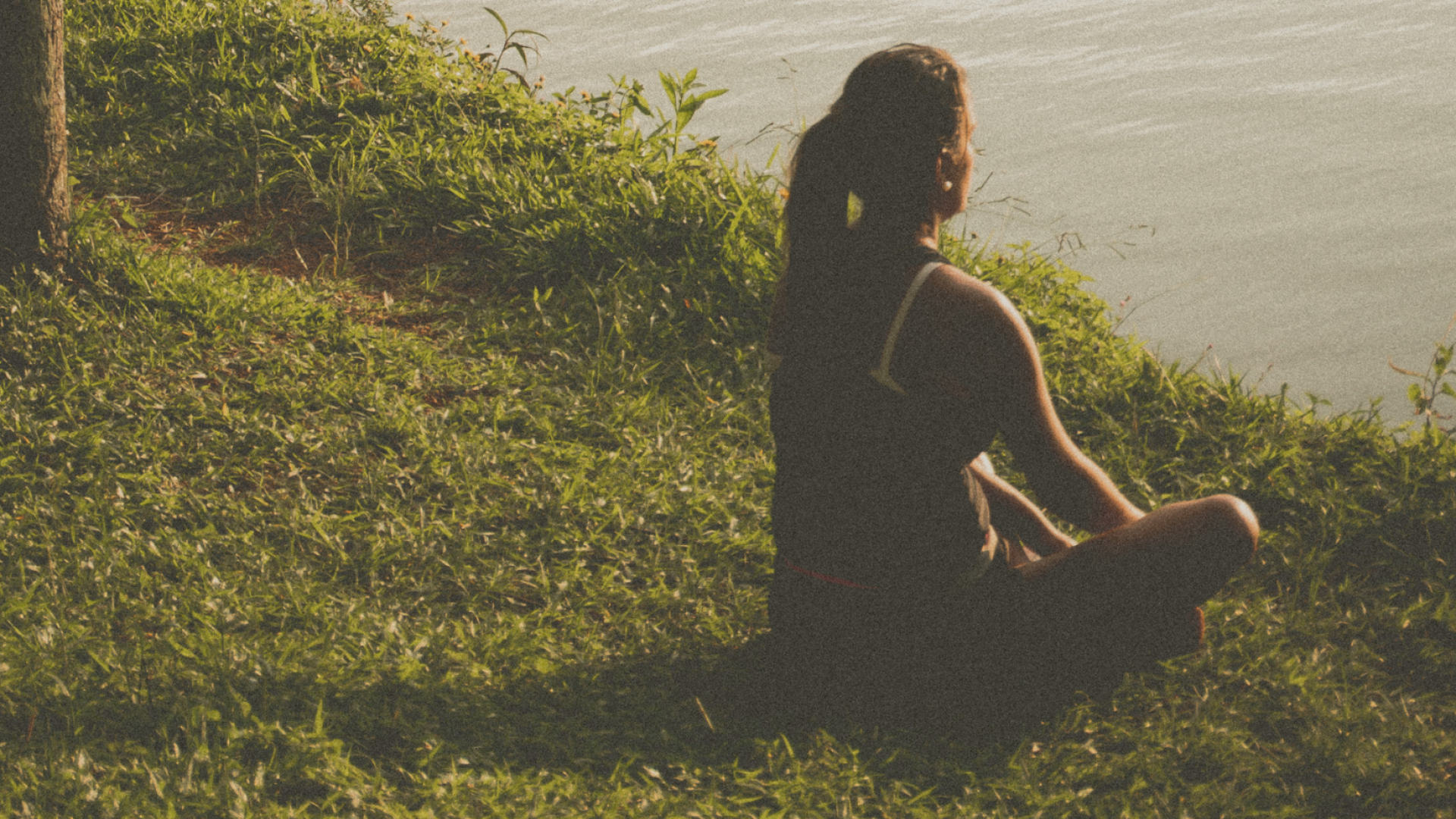 Persona medita al tramonto vicino all'acqua, serenità e pace interiore.
