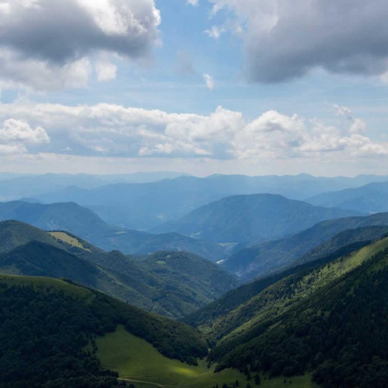 Panorama montano con colline verdi e cielo nuvoloso, atmosfera serena e rilassante.