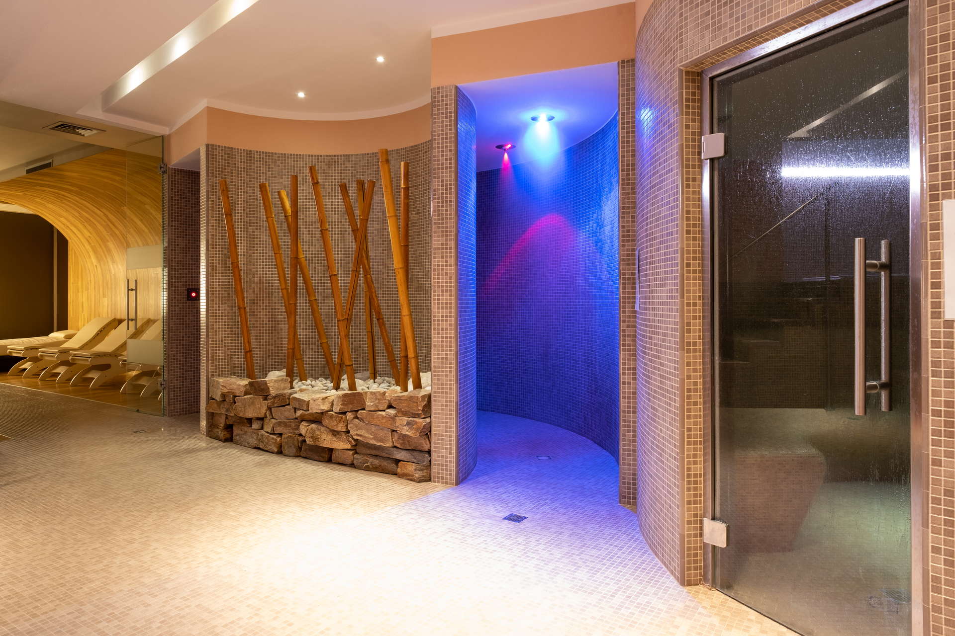 Spa moderna con luci colorate, bambù e sedie relax in legno.